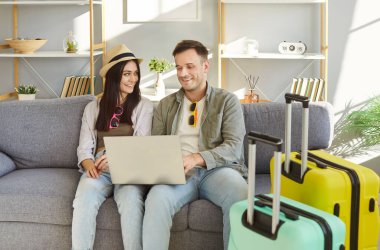 Mutlu turist çifti, seyahat etmek için dizüstü bilgisayarlı bavulları, tatil gezileri, balayı için büyük bavulları, hayalleri, yaz tatili plaj kıyafetleri giyip evden çevrimiçi seyahat etmeyi planlıyor.