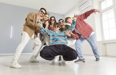 Gündelik giysiler giyen, güneş gözlüğü takan, geniş bir dans stüdyosunda poz veren, enerji, arkadaşlık ve dışavurumcu şehir kültüründen oluşan altı modayı takip eden neşeli genç bir grup. Eğlence ve hobi konsepti 