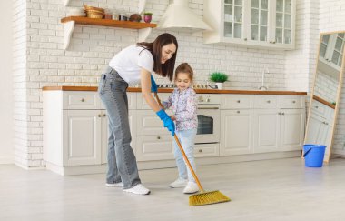 Gülümseyen anne ve tatlı kızı evde süpürgeyle yerleri süpürüyorlar. Genç bir kadın ebeveyn ve küçük bir çocuk evi temizliyor. Oda servisi ve aile işi konsepti.