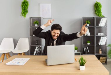 Mutlu iş adamının başarı ve zafer kutlamaları, heyecanlı kazananın enerjik tepkisi. Bilgisayarlı bir adam online mesaj kazanmak için masada oturuyor. İyi haber, coşku konsepti