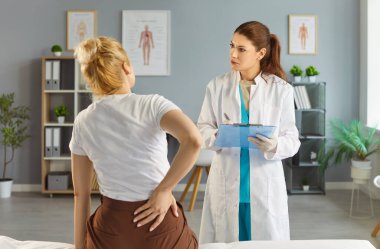 Klinikteki sağlık muayenesi sırasında sırt ağrısı çeken genç hasta kadın. Kadın doktor hastaların şikayetlerini dinliyor..