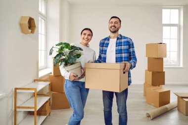 Mutlu genç aile çifti yeni bir daireye taşınıyor. Heyecanlı gülümseyen karı koca yeni evdeki karton kutuların arasında duruyor. Emlak, konut kredisi konsepti