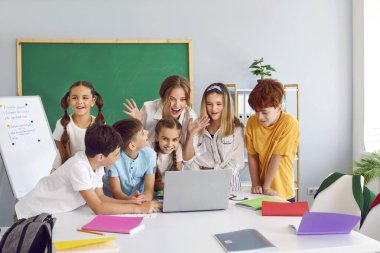 Küçük bir grup mutlu, pozitif, heyecanlı, zeki okul öğrencisinin neşeli öğretmenlerle dersi var, masadaki dizüstü bilgisayarda toplanıyorlar, yeni verilere bakıyorlar, ilginç oyunlar oynuyorlar, birlikte beceriler kazanıyorlar.