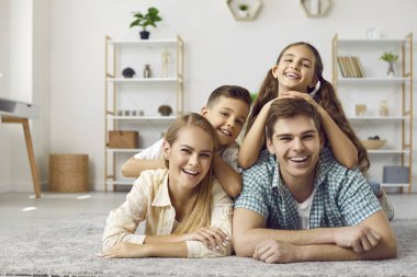Mutlu beyaz bir aile evde iki küçük çocuğuyla eğleniyor. Pozitif anne, baba, oğul ve kız portresi oturma odasında halının üzerinde birlikte yatıyor. Aile kavramı.