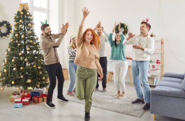 Mutlu genç insanlar gündelik kıyafetleriyle festival salonunda süslenmiş Noel ağacıyla dans ederek yeni yılı ev partisinde birlikte kutluyorlar. Kış tatili kavramı.