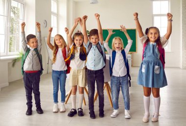 Çocukluk ve okul. İlkokuldan sınıf arkadaşlarının sınıfta eğlenirken çekilmiş bir portresi. Sırtlarında sırt çantaları olan gülümseyen kızlar ve oğlanlar ellerini kaldırarak sıraya girerler..