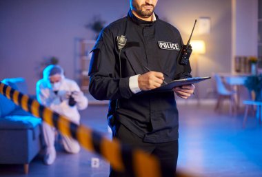 Üniformalı meçhul bir polis memuru protokole bilgi yazıp olay yerindeki barikat bantlarının yanındaki delilleri topluyor. Adli tıp uzmanı ipuçları toplamaya çalışıyor.