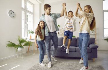 İki çocuklu mutlu bir aile birlikte oynuyor. Çocuk evde ailesinin elini tutarak kanepeden atlıyor. Anne, baba, oğul ve kız. Aile yaşam tarzı, aşk, eğlence konsepti.