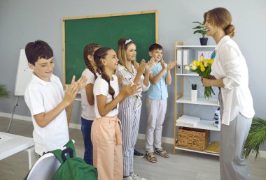 Okuldaki neşeli okul çocukları Uluslararası Öğretmenler Günü 'nde bayan öğretmenlerini tebrik ediyorlar. Genç erkekler ve kızlar öğretmenlerine bir buket çiçek verir ve neşeyle alkışlarlar..