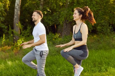 Genç zinde ve aktif bir çift doğada spor egzersizleri yapıyor. Spor giyim kuşamında gülen adam ve kadın parkta egzersiz yapıyorlar. Açık hava eğitimi ve spor konsepti.