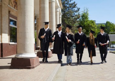 Bir grup mezun, ödül töreninden sonra kampüste yürürken konuşuyor. Havan ve bekarlığa veda kıyafetleri giymiş çok ırklı insanlar ellerinde diplomalarla dışarıda sıraya diziliyorlar.