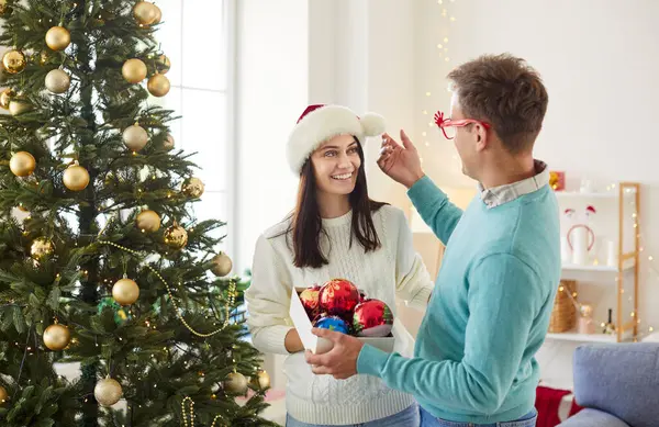 Genç ve mutlu bir çift oturma odasında durmuş Noel ağacını oyuncak toplarla süslüyorlar. Aşık erkek ve kadın yeni yıl kutlamasına hazırlanıyor. Kış tatili kavramı.