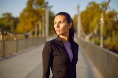 Spordan sonra parkta ayakta duran, spor egzersizleri ve doğadaki fitness eğitiminden sonra gülümseyen genç bir sporcunun portresi. Açık hava sporu ve sağlıklı yaşam tarzı konsepti.