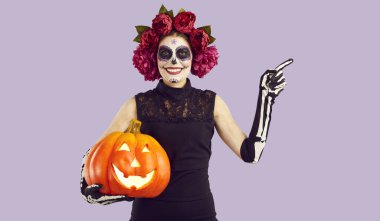 Cadılar Bayramı için yüzü boyanmış genç ve güzel bir kadın elinde korkunç bir balkabağı tutuyor. Kırmızı şakayık desenli çelenk, siyah elbise ve işaret parmağıyla gösterilen iskelet eldivenli kızın portresi.