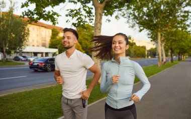Aktif formda sportif bir çift, şehir kaldırımında enerjik bir şekilde koşuyor, şehir binalarının ve arabaların yakınında koşuyor, dışarıda egzersiz yapıyor, aktif bir yaşam tarzı yaşıyor, aile sporu rutini yapıyor. 