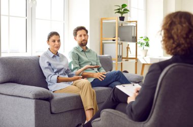 Evli çift terapi seansı yapıyor. Kadın ve erkek bir koltukta oturup profesyonel bir terapist ya da aile psikologu ile olan ilişkilerini konuşuyorlar.