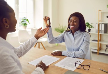 Mutlu, dost canlısı, gülümseyen Afrikalı Amerikalı kadın emlakçı ya da emlakçı ofiste bir sözleşme imzaladıktan sonra ev anahtarlarını mutlu müşterisine veriyor.