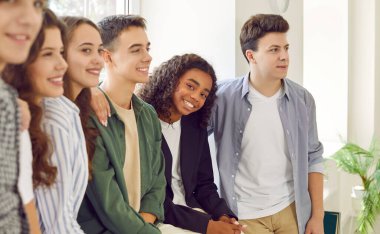 Okul etkinliğine katılan bir grup mutlu çok ırklı erkek ve kız çocuğu. Neşeli genç Afrikalı Afrikalı Amerikalı kız okul sahnesine yan yana bakan arkadaşlarıyla kameraya gülümsüyor.