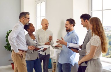 Olumlu çok ırklı meslektaşlar pencerenin önünde sohbet ediyorlar. Dizüstü bilgisayarları ve dizüstü bilgisayarları olan bir grup insan başlangıç projesini tartışıyor. Birlikte çalışma, takım çalışması konsepti.