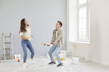 Gülümseyen mutlu çift yeni dairelerinin duvarlarını boyarken eğleniyor. Evli bir adam ve kadın tadilat yapıyor. Yeni bir daireye taşınmaya hazırlanıyorlar..