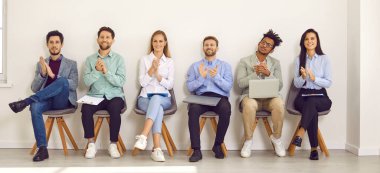 Genç profesyonel iş adamları arka arkaya koltuklarda oturup kameraya bakıyorlar ve alkışlıyorlar. Özgeçmişleri ve dizüstü bilgisayarları olan iş adayları veya toplantıda bir grup personel arayanlar. Pankart.