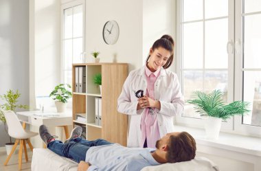 Genç doktor portresi. Muayene odasında hasta bir adama danışmanlık yapıyor. Erkek hasta, sağlık kontrolü için klinikte kanepede yatıyor. Sağlık ve Tıp Konsepti.