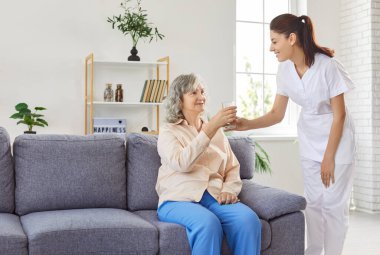 Nazik bir hemşire, yaşlı bir kadına su veren yaşlı bir bakıcı bakımevinde ikamet eden yaşlı bir yetişkin, bakım hizmetlerini ziyaret eden bir bayan doktor, yardım eden bir yardımcı.