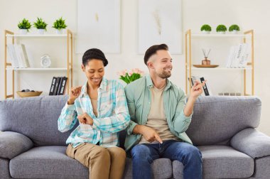 Mutlu, genç ve değişik kıyafetleri olan çift oturma odasındaki kanepede oturup eğleniyor. Neşeli erkek ve kadın bayramı kutluyor, taşınıyor ya da birlikte iyi bir ruh halinin tadını çıkarıyor..