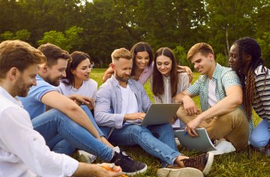 Mutlu çok ırklı arkadaşlar yeşil parkta oturur, modern dizüstü bilgisayar kullanır, iş araştırma grubu projesinde birlikte çalışır, başarılı bilim öğrencileri yarışması için dijital başvuru formu doldururlar.