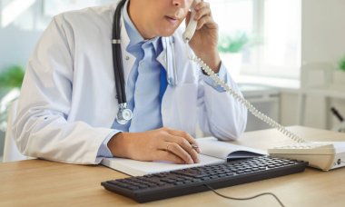 Profesyonel doktor, ofis masasındaki erkek hemşire, telefonla konuşuyor, danışmanlık defteri, profesyonel iletişim ve bilgi yönetimi, hastaya klinik veya idari yardım 