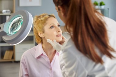 Dermatolog, güzellik uzmanı ya da kozmetik uzmanı klinikte büyüteç aynası kullanan kadın yüzü, laboratuvar önlüğü giyen hemşire, eldiven giyen, sağlık kontrolü yapan hasta, dermatoloji uzmanı.