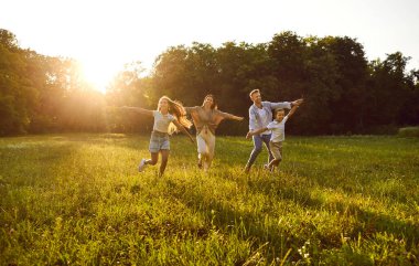 Mutlu aile oyunu ve doğada eğlenmek. Neşeli, neşeli anne, baba ve çocuklar sıcak, güneşli bir yaz akşamında çimenli bir çimenlikte birlikte koşuyorlar.