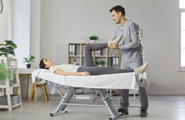 Profesyonel fizyoterapist, kanepede yatan kadına bacak masajı yapıyor, acıyla başa çıkmada yardımcı oluyor, klinikte manüel terapi yapıyor, vücut sağlığını korumaya yardım ediyor.