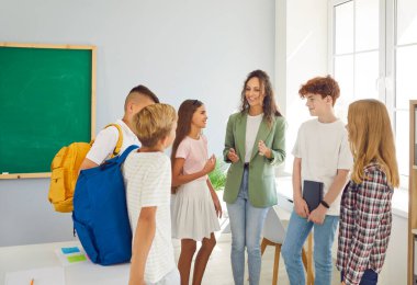 Bir grup mutlu okul çocuğu ve genç, dost canlısı bayan öğretmenleri sınıfta bir çemberin içinde duruyorlar ve dersten sonra konuşuyorlar. Okula, eğitime ve bilgiye dönüş konsepti.