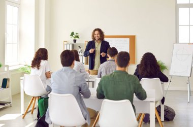 Lisedeki erkek arkadaş canlısı gülümseme öğretmeni. Genç üniversite öğrencileri ve sınıf arkadaşları masada oturup sınıfta çalışıyorlar. Eğitim, bilgi ve okul konseptine geri dönüş.