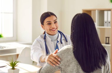 Gülümseyen dost canlısı doktor portresi hastaların omuzlarına dokunuyor steteskop takıyor ve danışmanlık yapıyor. Klinikte tıbbi muayene sırasında arkasına yaslanıp doktorunu dinleyen bir kadın..