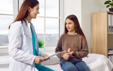 Çocuk klinikte ya da hastanede doktorla konuşuyor. Çocuk hasta, çocuk doktoruyla güvenilir bir konuşma yapıyor. Küçük kız, kadın doktorla birlikte tıp yatağında oturuyor, sorular soruyor ve cevaplıyor.