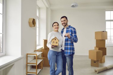 Genç bir çift yeni bir daireye taşınıyor. Karton kutularla oturma odasında elinde oyuncak ev, anahtar ve gülümsemeyle mutlu bir adam ve kadın. Emlak kavramı