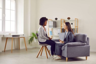 Kadın terapist ya da psikologdan yardım ve destek alıyor. Genç Afro-Amerikalı kız sandalyede oturuyor ve kanepede pano ile oturan terapistle konuşuyor. Terapi, psikoterapi konsepti
