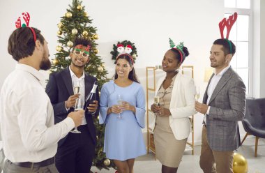 Çok uluslu gülümseyen insanlar meslektaşlarını bir kadeh şampanyayla dinlerler ve kadeh kaldırırlar. Klasik kıyafetler giymiş ve kafalarında komik boynuzlar olan arkadaşlar bayramı ofiste kutluyorlar..