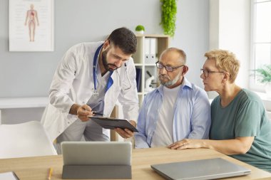 Doktor danışma klinikteki yaşlı çiftin tıbbi kayıtlarını inceler, sağlık testi sonuçlarını karşılar. Yaşlı, olgun hastalar doktorlarla tedaviyi tartışıyor. Tıp konsepti. 