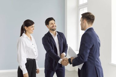 Profesyonel emlakçı mutlu çifte yeni bir daire gösteriyor. Takım elbiseli kadın ve erkek boş bir odada duruyor, yeni bir ev alıyor, ev sahibi oluyor, emlakçıyla el sıkışarak anlaşmalar yapıyor..