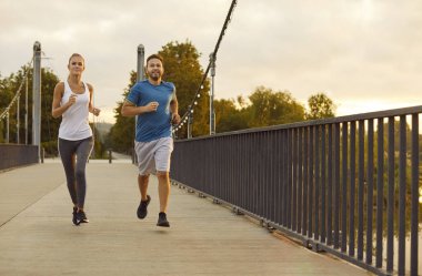 Akşamları iki koşucu. Genç erkek arkadaş ve kız arkadaş şehir sokaklarında koşu yapıyorlar. Spor giyimli spor kankalar köprü çitleri boyunca birlikte koşuyorlar. Spor, egzersiz konsepti