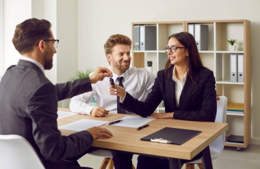 Profesyonel bir emlakçı, ofiste oturan bir kadın müşteriye ev anahtarını veriyor. Genç çift bir emlakçıyla anlaşmaya vardı, emlak ve araba satın almanın keyfini çıkaran bir sözleşme imzaladılar..