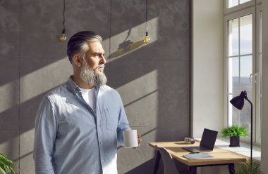 Olgun sakallı çekici bir iş adamının portresi. Ofisinin yanında elinde bir fincan çay ya da kahveyle duruyor ve moladan dinlenirken sakince pencereye bakıyor..