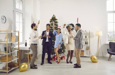 Ofisteki yeni yıl partisinde çok uluslu gençler şampanya kadehleriyle dans ediyorlar. Klasik kıyafetler giyiyorlar ve kafalarında komik boynuzlar var. Şirket partisinde eğlenceli bir kutlama..