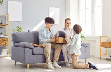 Küçük ve genç oğlu olan mutlu anne eve yeni bir paket bırakıyor kanepeye birlikte oturuyor, gülümsüyor anne ve çocuk aletle eğleniyor, hafta sonları hediye alıyor. 