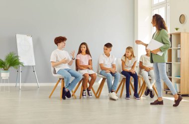 Çocuk psikoloğu. Bir grup ilkokul çocuğu için psikolojik eğitim veren arkadaş canlısı genç bir kadın sınıfta sıraya girip erkek arkadaşlarını dinliyor..