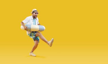 Güneş gözlüklü, lastik yüzük takan ve stüdyo sarısı arka planda izole edilmiş eğlenen neşeli bir adamın tam vücut fotoğrafı. Komik turist yaz tatiline çıkıyor. Tatil ve seyahat kavramı.