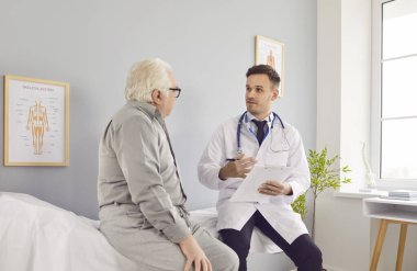 Tıp bürosundaki yaşlı, gri saçlı bir hastanın portresi elinde randevu ile rapor tutan ve klinikteki tıbbi muayene sırasında danışmanlık yapan erkek doktoru dinliyor..